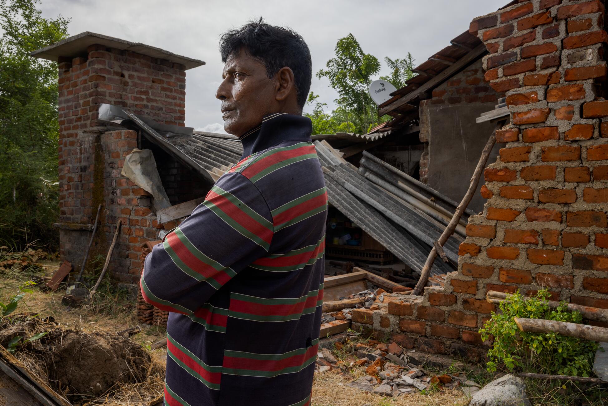 Picture of a man standing outside a brick house with a collapsed roof and walls