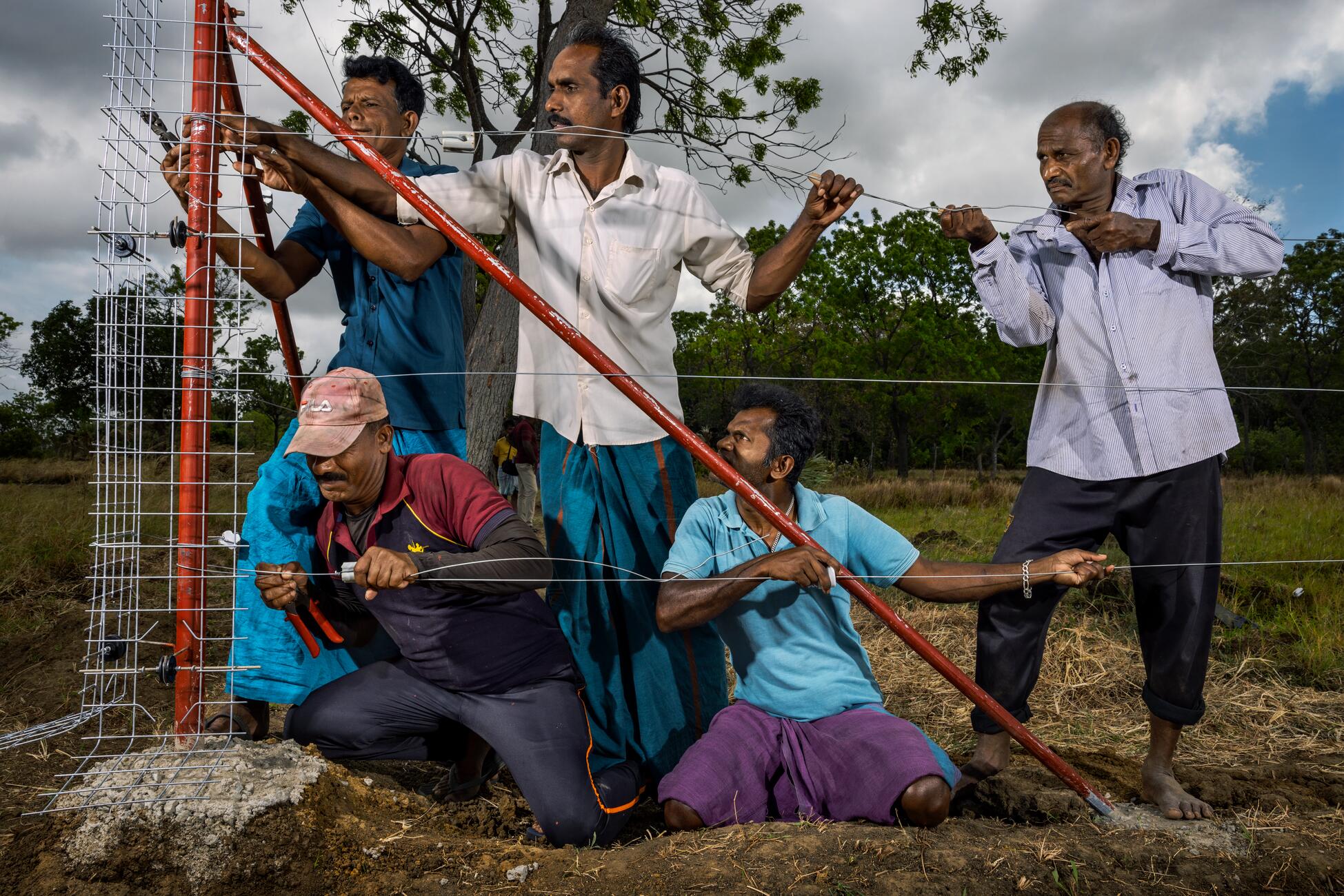 Picture of five men attaching wires to a fence outside in a field